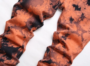 Dettaglio dei jeans da uomo con motivo tie-dye arancione e nero e cuciture bianche