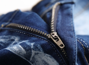 Macro shot of durable metal zipper and yellow stitching on washed dark blue denim jeans