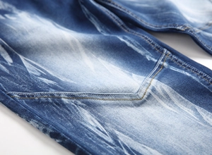 Detail of dark blue denim jeans showing heavy wash distress and yellow contrast stitching
