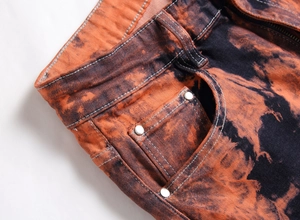 Dettaglio macro di jeans da uomo con lavaggio tie-dye arancione e nero e rivetti