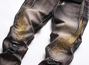 Detail of grey distressed jeans with gold wing embroidery and metallic studs