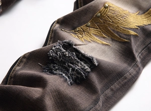 Detail of distressed denim jeans featuring gold wing embroidery and metal rivets