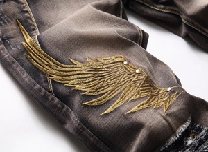 Detailed close-up of golden wing embroidery with metallic rivets on distressed brown jeans