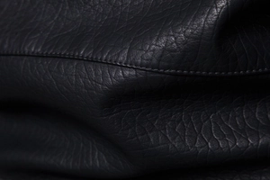 Detail macro shot of black lychee grain PU leather with precise reinforced stitching