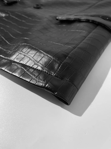 Macro close-up showing the detailed black crocodile embossed texture of the faux leather jacket