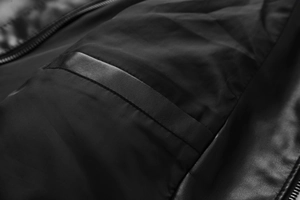 Close-up detail of smooth black nylon fabric with textured leather trim and zipper