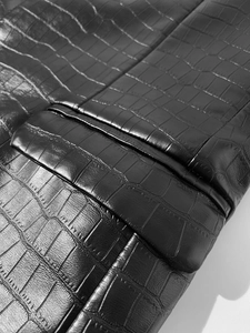 Macro shot of black crocodile embossed faux leather texture with precise stitching detail