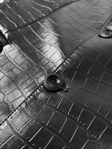Close-up detail of crocodile embossed PU leather texture and button on men's jacket