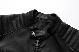 Detail of a black biker jacket featuring a stand collar, snap button, and quilted shoulders