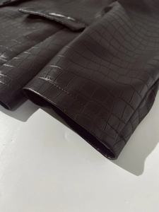 Detail of crocodile embossed faux leather jacket showing stitching on pocket and cuff