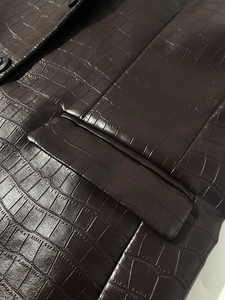 Detailed macro view of dark brown croc-embossed leather jacket with pocket and button