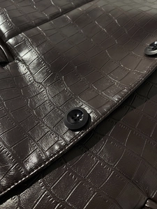 Detailed view of dark brown crocodile embossed faux leather fabric and black round button