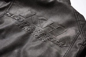 Close-up of embossed DKH logo and quilted stitching on black faux leather biker jacket