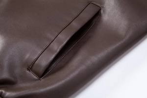 Close-up of deep brown PU leather jacket pocket showing fine grain texture and neat stitching