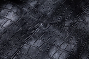 Macro detail of black crocodile embossed faux leather jacket texture and stitching