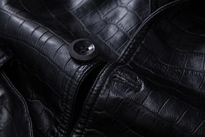 Close-up of black crocodile embossed faux leather texture with button detail and stitching