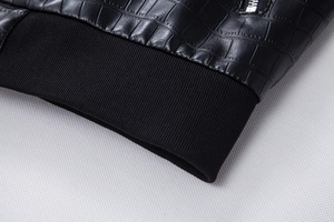 Close-up of black crocodile-embossed faux leather jacket with ribbed knit cuffs