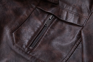 Detail of dark brown faux leather jacket featuring a metal zipper pocket and double stitching