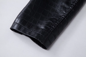 Detailed macro view of black faux leather jacket cuff with crocodile embossed texture