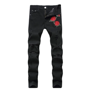 Detail of red rose embroidery and distressed ripped holes on men's black slim denim jeans