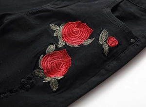 Macro detail of red rose embroidery and distressed ripped texture on black men's denim