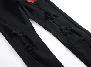Detail of black ripped jeans for men featuring red rose embroidery and distressed texture