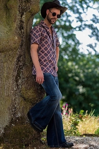 Outdoor male model wearing retro floral shirt and deep blue flare jeans in a forest setting