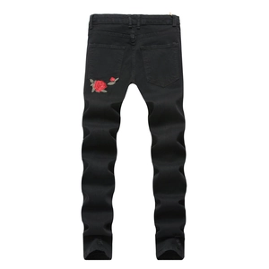 Detail of red rose embroidery and distressed hem on men's slim black denim jeans