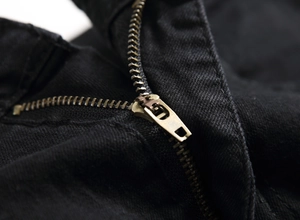 Close-up of bronze-tone metal zipper on black twill denim trousers with sharp texture