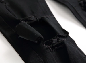 Close-up detail of distressed knee rips and frayed edges on black slim denim jeans