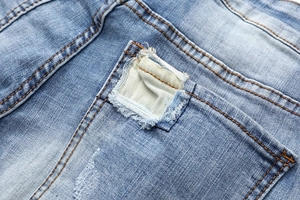 Close-up of light blue distressed denim jeans showing ripped patches and orange stitching