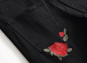 Detail of red rose floral embroidery on the back pocket of black denim jeans