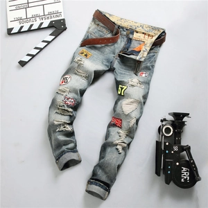 Detail of men's distressed straight jeans with vintage badges and worn out hole effects
