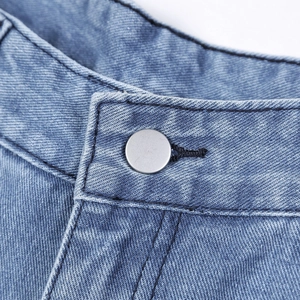 Close-up of matte silver metal button and neat stitching on blue high-waisted denim jeans