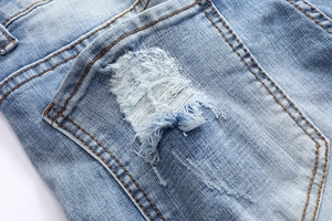 Detail of light blue denim jeans with orange stitching and distressed pocket texture