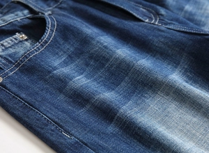 Detail of dark blue denim jeans with white contrast stitching and metal rivet reinforcement