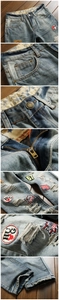 Detail of distressed denim pants with embroidered patches, metal button and rustic zipper