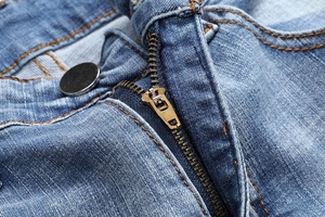 Detailed close-up of blue denim jeans featuring a brass zipper and metal button closure