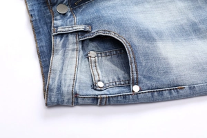Close-up of light blue denim jeans showing metal button, rivets, and orange stitching detail