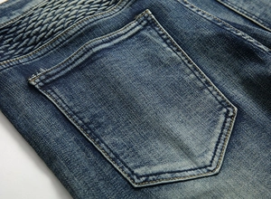 Détail du jean bleu délavé avec plis matelassés style motard et poche arrière classique