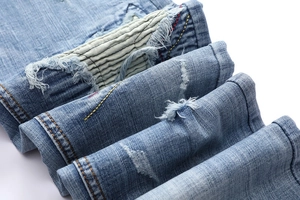 Detail of distressed light blue denim jeans with vintage whiskers and striped fabric patches