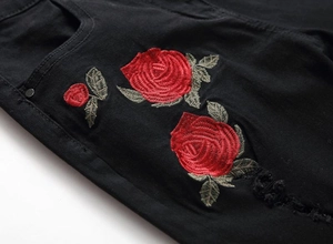 Men's black ripped jeans featuring vibrant red rose embroidery and distressed denim texture