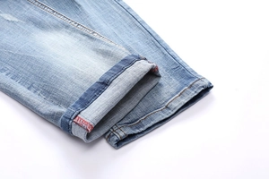 Detailed close-up of light blue denim jeans cuff showing bright red overlock stitching