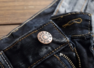 Détail du bouton en cuivre vintage avec gravure sur un jean en denim noir délavé