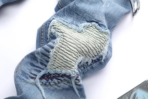 Macro view of distressed light blue denim jeans with white pleated knee repair details