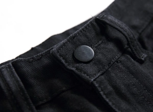 Gros plan du bouton en métal noir mat et texture sergée du jean de motard homme