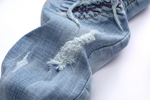 Detail of light blue distressed denim with heavy ripped holes and dual-color embroidery