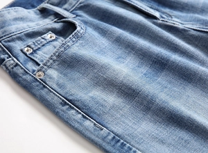 Macro detail of men's blue denim shorts showing silver metal rivets and washed texture