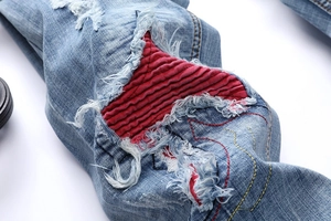 Close-up of distressed denim jeans featuring red corduroy patches and contrast stitching