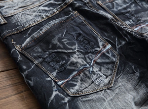 Détail de la poche arrière déchirée sur jean noir pour homme avec coutures orange et bleu
